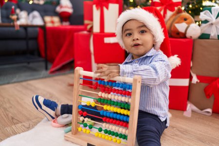 Photo for Adorable hispanic toddler playing with abacus sitting on floor by christmas gifts at home - Royalty Free Image