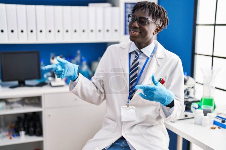 Téléchargez les photos : Homme afro-américain scientifique souriant confiant parlant au laboratoire - en image libre de droit