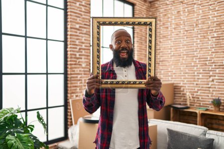 Foto de Hombre afroamericano poniendo la cara en un marco vacío celebrando loco y sorprendido por el éxito con los ojos abiertos gritando emocionado. - Imagen libre de derechos