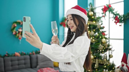 Photo for Young chinese woman celebrating christmas holding glass of champagne having video call at home - Royalty Free Image