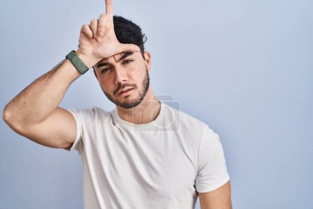 Photo for Hispanic man with beard standing over white background making fun of people with fingers on forehead doing loser gesture mocking and insulting. - Royalty Free Image