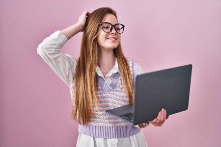 Téléchargez les photos : Jeune femme caucasienne travaillant à l'aide d'un ordinateur portable souriant confiant toucher les cheveux avec geste de la main vers le haut, posant attrayant et à la mode - en image libre de droit