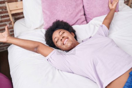 Foto de Mujer afroamericana despertando estirando brazos en el dormitorio - Imagen libre de derechos