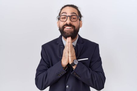 Photo for Hispanic man with beard wearing suit and tie praying with hands together asking for forgiveness smiling confident. - Royalty Free Image