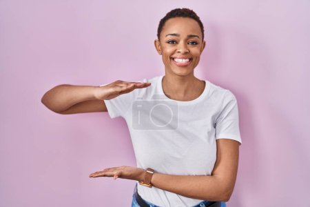 Photo for Beautiful african american woman standing over pink background gesturing with hands showing big and large size sign, measure symbol. smiling looking at the camera. measuring concept. - Royalty Free Image