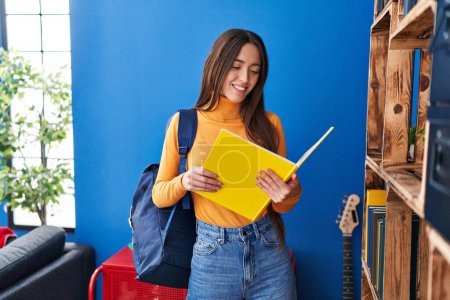 Téléchargez les photos : Jeune belle étudiante hispanique portant sac à dos livre de lecture à la maison - en image libre de droit