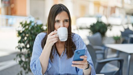 Téléchargez les photos : Young beautiful hispanic woman using smartphone drinking coffee at coffee shop terrace - en image libre de droit
