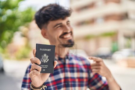 Photo for Young hispanic man pointing with finger to united states passport at street - Royalty Free Image