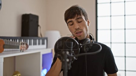 Téléchargez les photos : Passionné jeune homme hispanique littéralement vivre la musique, emporté dans la mélodie tout en portant des écouteurs et en chantant son cœur dans un studio - en image libre de droit