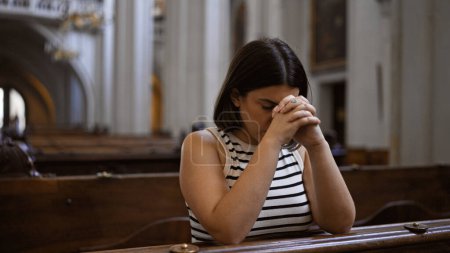Foto de Joven mujer hispana hermosa rezando en un banco de la iglesia en la iglesia agustiniana de Viena - Imagen libre de derechos