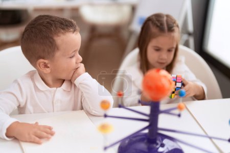 Foto de Adorable chica y niño jugando con el cubo de rompecabezas de color sentado en la mesa en el jardín de infantes - Imagen libre de derechos
