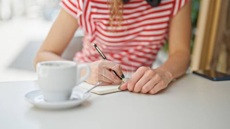 Photo for Young blonde woman sitting on table writing on notebook at coffee shop terrace - Royalty Free Image