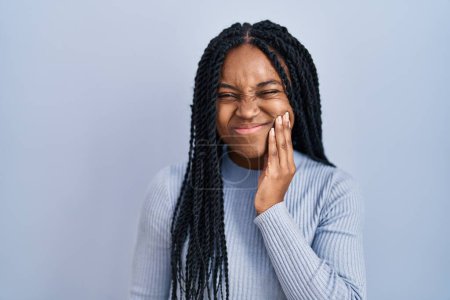 Téléchargez les photos : Femme afro-américaine debout sur fond bleu touchant la bouche avec une expression douloureuse à cause de maux de dents ou de maladies dentaires sur les dents. dentiste - en image libre de droit
