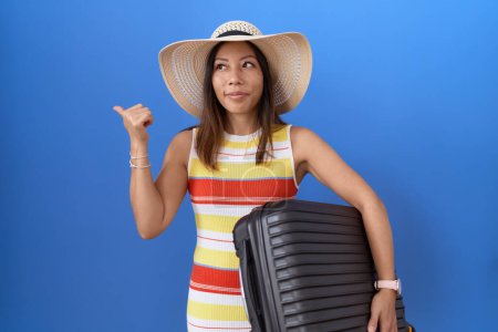 Photo for Middle age chinese woman holding suitcase going on summer vacation pointing thumb up to the side smiling happy with open mouth - Royalty Free Image