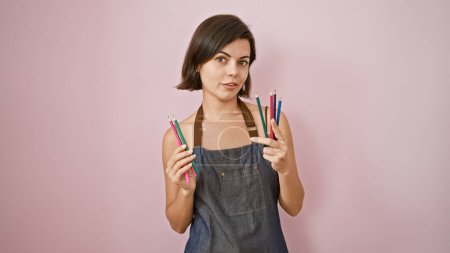 Foto de Joven hermosa artista hispana sosteniendo lápices de color sobre fondo rosa aislado - Imagen libre de derechos