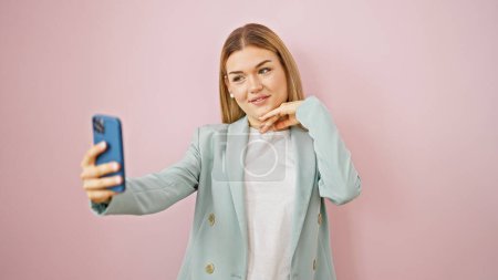 Téléchargez les photos : Jeune femme blonde ouvrière souriante confiante faire selfie par smartphone sur fond rose isolé - en image libre de droit