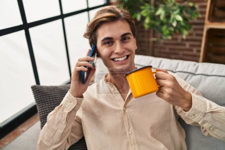Téléchargez les photos : Jeune homme caucasien parlant sur smartphone boire du café à la maison - en image libre de droit