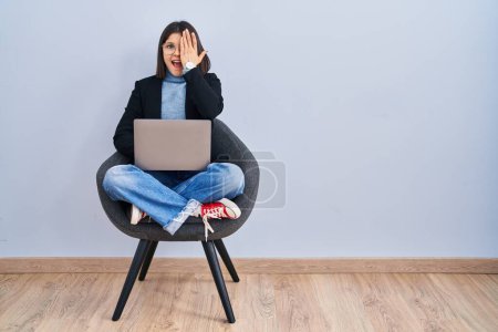 Photo for Young hispanic woman sitting on chair using computer laptop covering one eye with hand, confident smile on face and surprise emotion. - Royalty Free Image