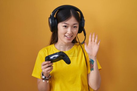 Foto de Chino joven mujer jugando videojuego celebración controlador renuncia decir hola feliz y sonriente, gesto de bienvenida amistoso - Imagen libre de derechos