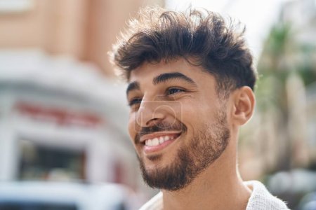 Téléchargez les photos : Jeune homme arabe souriant confiant regardant du côté de la rue - en image libre de droit