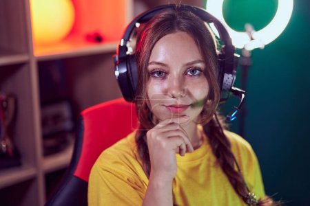 Photo for Young blonde woman streamer sitting on table with relaxed expression at gaming room - Royalty Free Image