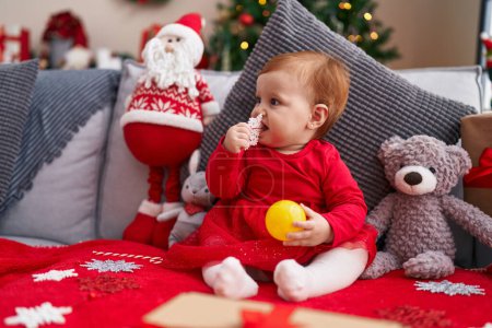 Foto de Adorable pelirroja niño chupando la decoración de la estrella de Navidad sentado en el sofá en casa - Imagen libre de derechos