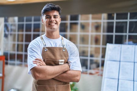 Téléchargez les photos : Jeune homme hispanique serveur souriant confiant debout avec les bras croisés geste à la terrasse du café - en image libre de droit