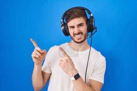 Photo for Hispanic man with beard listening to music wearing headphones pointing aside worried and nervous with both hands, concerned and surprised expression - Royalty Free Image