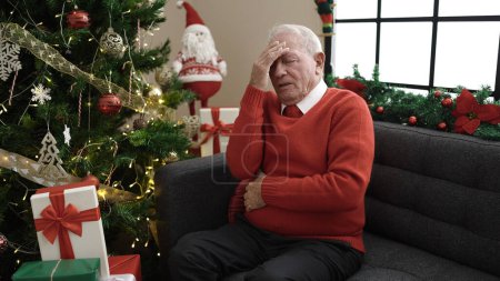 Téléchargez les photos : Maux d'estomac des personnes âgées assis près de l'arbre de Noël à la maison - en image libre de droit