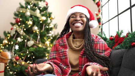Photo for African woman smiling sitting by christmas tree at home - Royalty Free Image