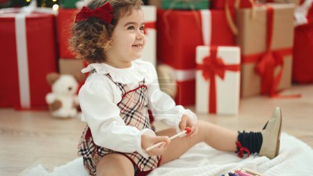 Photo for Adorable hispanic girl playing xylophone sitting on floor by christmas tree at home - Royalty Free Image