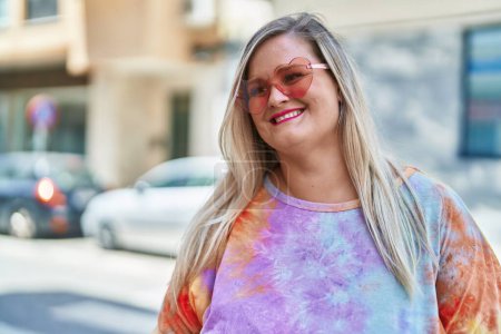 Foto de Mujer joven sonriendo confiada usando gafas de sol de corazón en la calle - Imagen libre de derechos