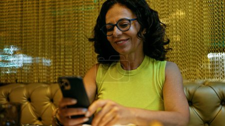 Foto de Mujer hispana de mediana edad usando smartphone en un restaurante - Imagen libre de derechos