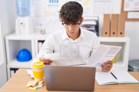 Foto de Joven adolescente hispano trabajador de negocios utilizando el documento de lectura portátil en la oficina - Imagen libre de derechos