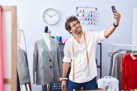 Téléchargez les photos : Young hispanic man tailor smiling confident make selfie by smartphone at clothing factory - en image libre de droit