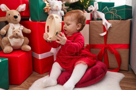 Photo for Adorable redhead toddler playing tambourine sitting on floor by christmas gifts at home - Royalty Free Image