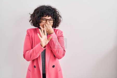 Téléchargez les photos : Femme hispanique avec les cheveux bouclés debout sur fond isolé sentant quelque chose puant et dégoûtant, odeur intolérable, retenant souffle avec les doigts sur le nez. mauvaise odeur - en image libre de droit