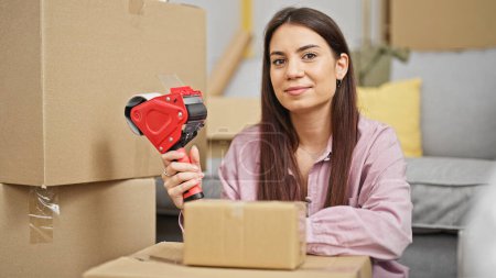 Photo for Young beautiful hispanic woman smiling confident packing cardboard box at new home - Royalty Free Image
