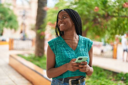Téléchargez les photos : Femme afro-américaine souriante confiante en utilisant un smartphone au parc - en image libre de droit