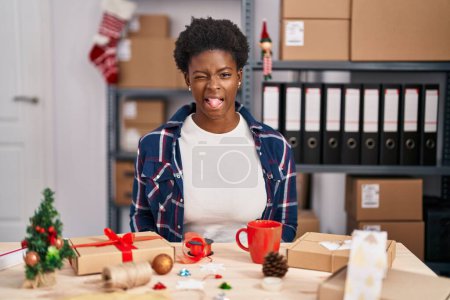 Photo for African american woman working at small business doing christmas decoration sticking tongue out happy with funny expression. emotion concept. - Royalty Free Image