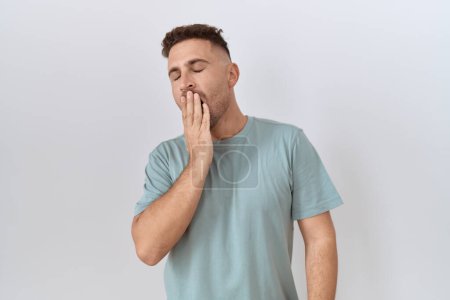 Foto de Hombre hispano con barba de pie sobre fondo blanco aburrido bostezo cansado cubriendo la boca con la mano. inquietud y somnolencia. - Imagen libre de derechos