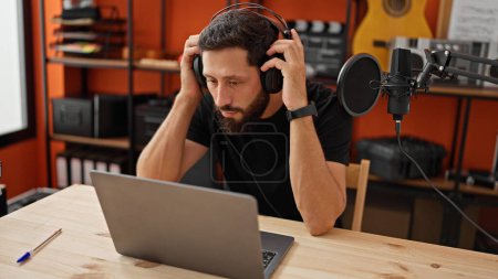 Foto de Joven músico hispano escuchando música usando laptop en estudio de música - Imagen libre de derechos