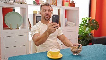 Téléchargez les photos : Jeune homme prenant le petit déjeuner faisant appel vidéo à la salle à manger - en image libre de droit