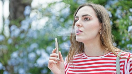 Téléchargez les photos : Jeune femme blonde fumeur vaper au parc - en image libre de droit