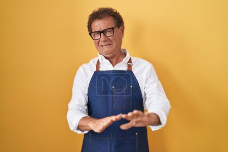 Photo for Middle age hispanic man wearing professional cook apron disgusted expression, displeased and fearful doing disgust face because aversion reaction. with hands raised - Royalty Free Image