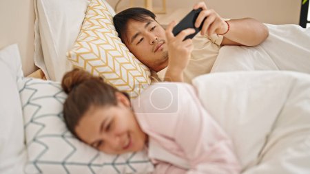 Téléchargez les photos : Homme et femme couple couché sur le lit en utilisant des smartphones dans la chambre - en image libre de droit