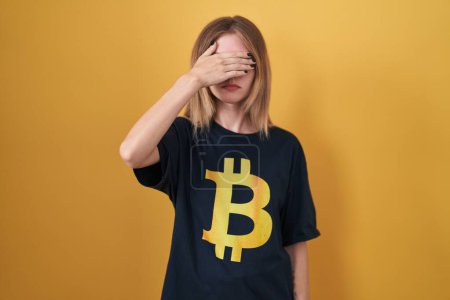 Photo for Blonde caucasian woman wearing bitcoin t shirt covering eyes with hand, looking serious and sad. sightless, hiding and rejection concept - Royalty Free Image