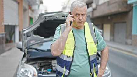 Téléchargez les photos : Moyen âge homme aux cheveux gris parler sur smartphone avec assurance pour panne de voiture à la rue - en image libre de droit