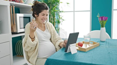 Photo for Young pregnant woman having breakfast watching video on touchpad at dinning room - Royalty Free Image