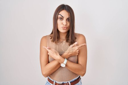 Photo for Young hispanic woman standing over white background pointing to both sides with fingers, different direction disagree - Royalty Free Image